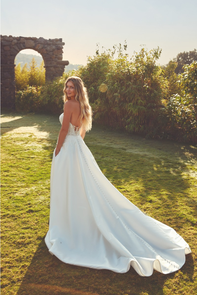 Abito da sposa VALLEY di Eddy K, modello elegante con strascico, indossato in un giardino al tramonto.