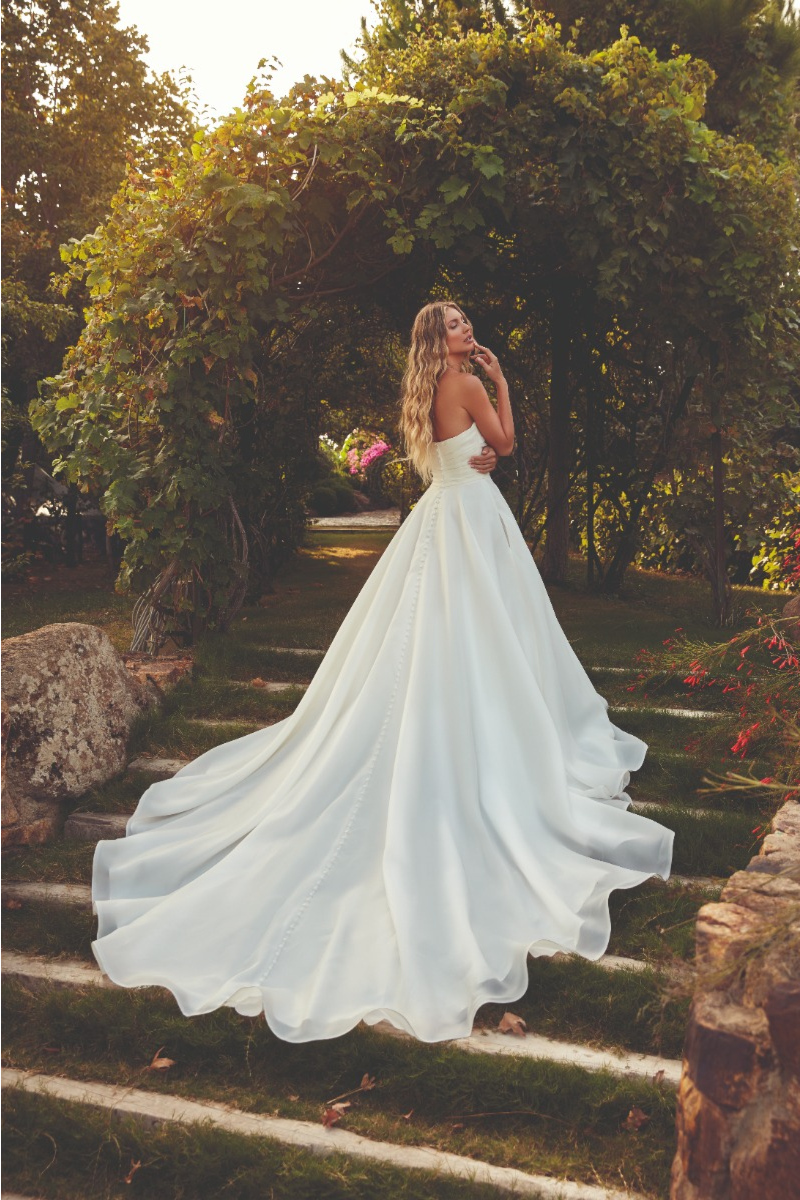 Abito da sposa TEAGAN Eddy K, scollo a cuore, lungo strascico, ambientato in un giardino romantico.