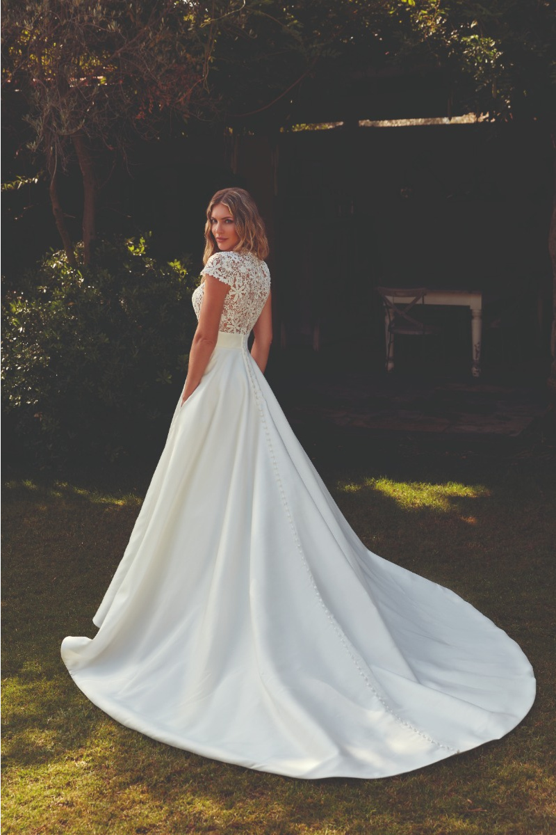 Abito da sposa Connie Eddy K con corpetto in pizzo e gonna lunga, ambientato in un giardino ombreggiato.