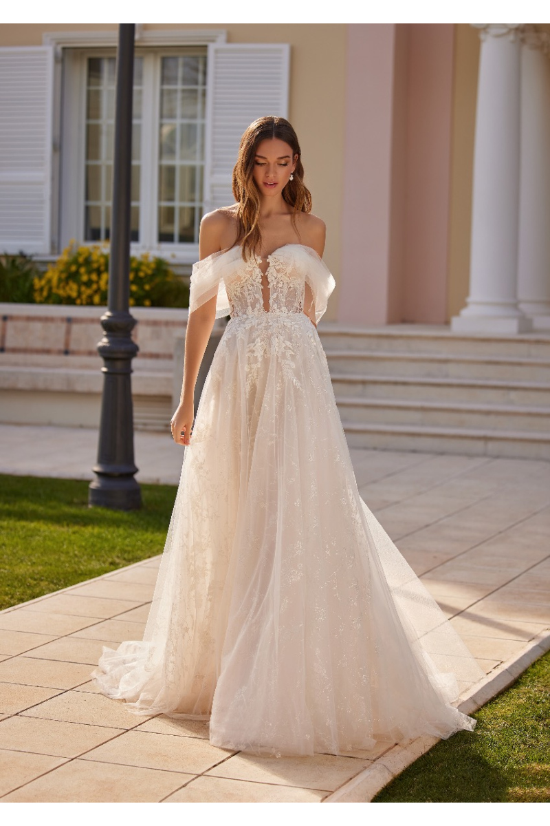 Abito da sposa Ennia in pizzo bianco, scollo a cuore, ambientazione esterna elegante.