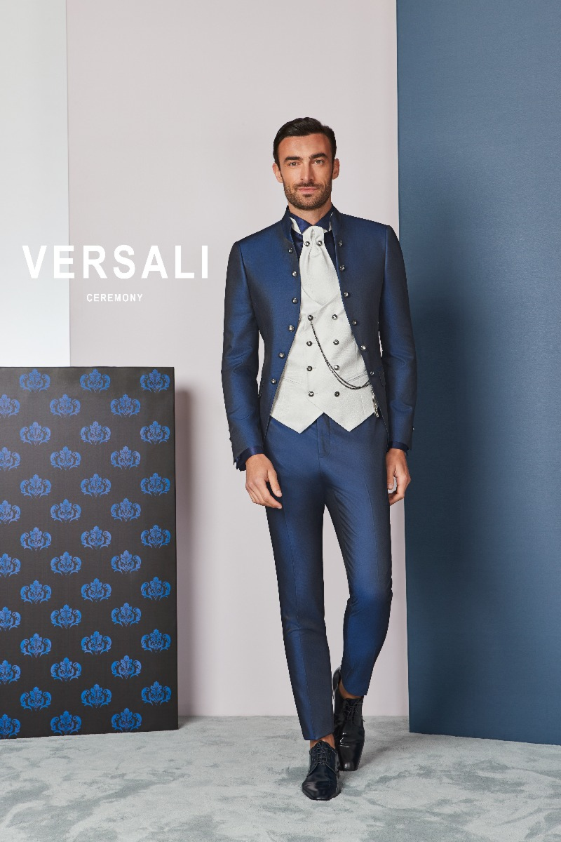 Abito da cerimonia uomo FIT 42 blu Versali, giacca elegante e gilet bianco, sfondo geometrico.