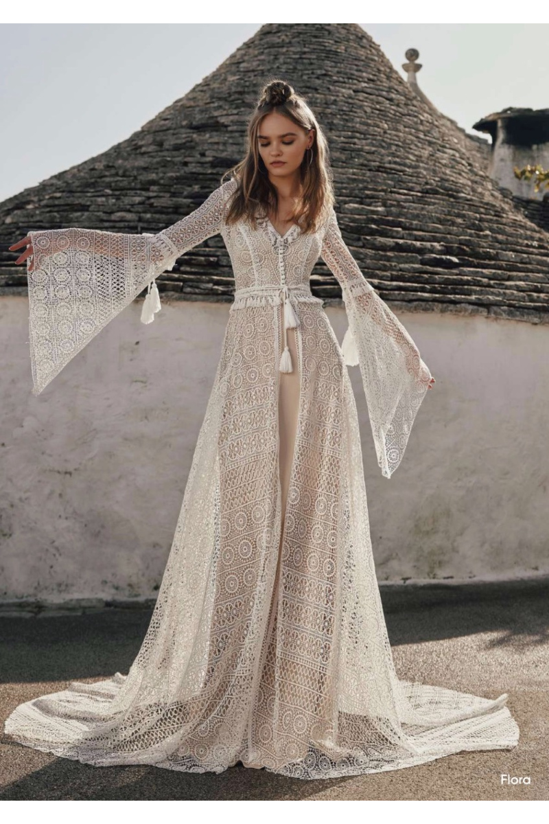 Abito boho in pizzo bianco con maniche ampie, sfondo architettura tradizionale.