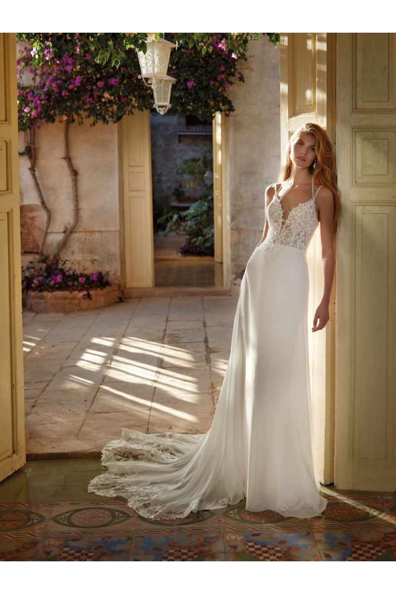 Abito da sposa HALLIE Nicole Colet con corpetto in pizzo e gonna fluente, ambientato in un cortile elegante.