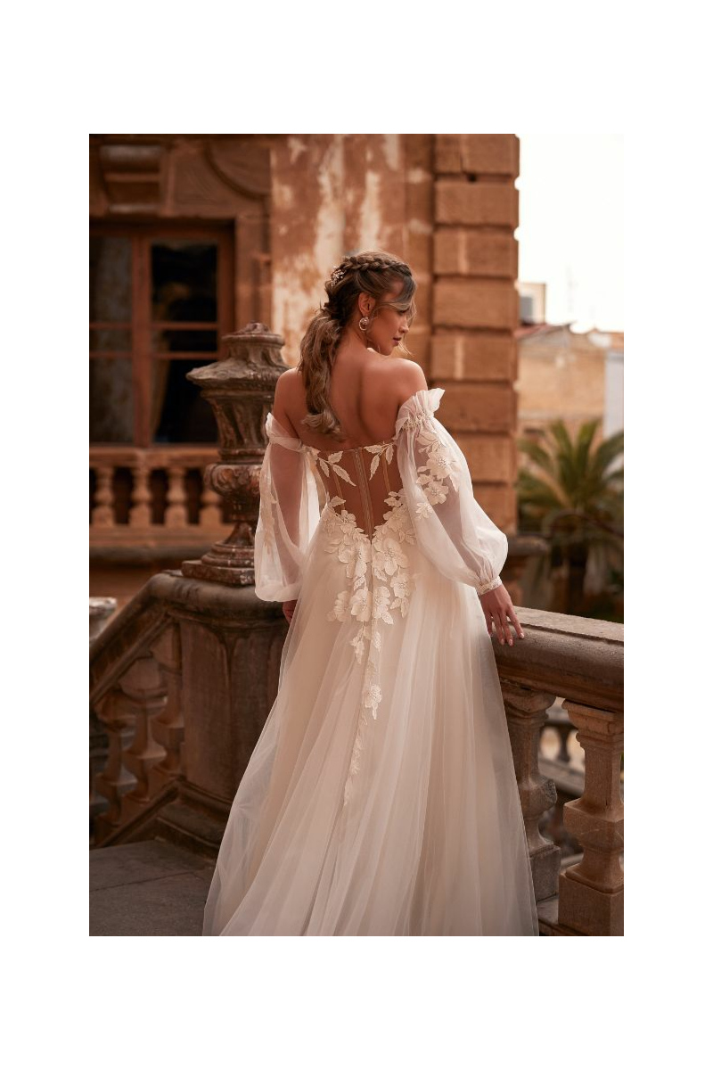 Abito da sposa Hermiona Dama, schiena scoperta, dettagli floreali, maniche trasparenti, ambientazione romantica.