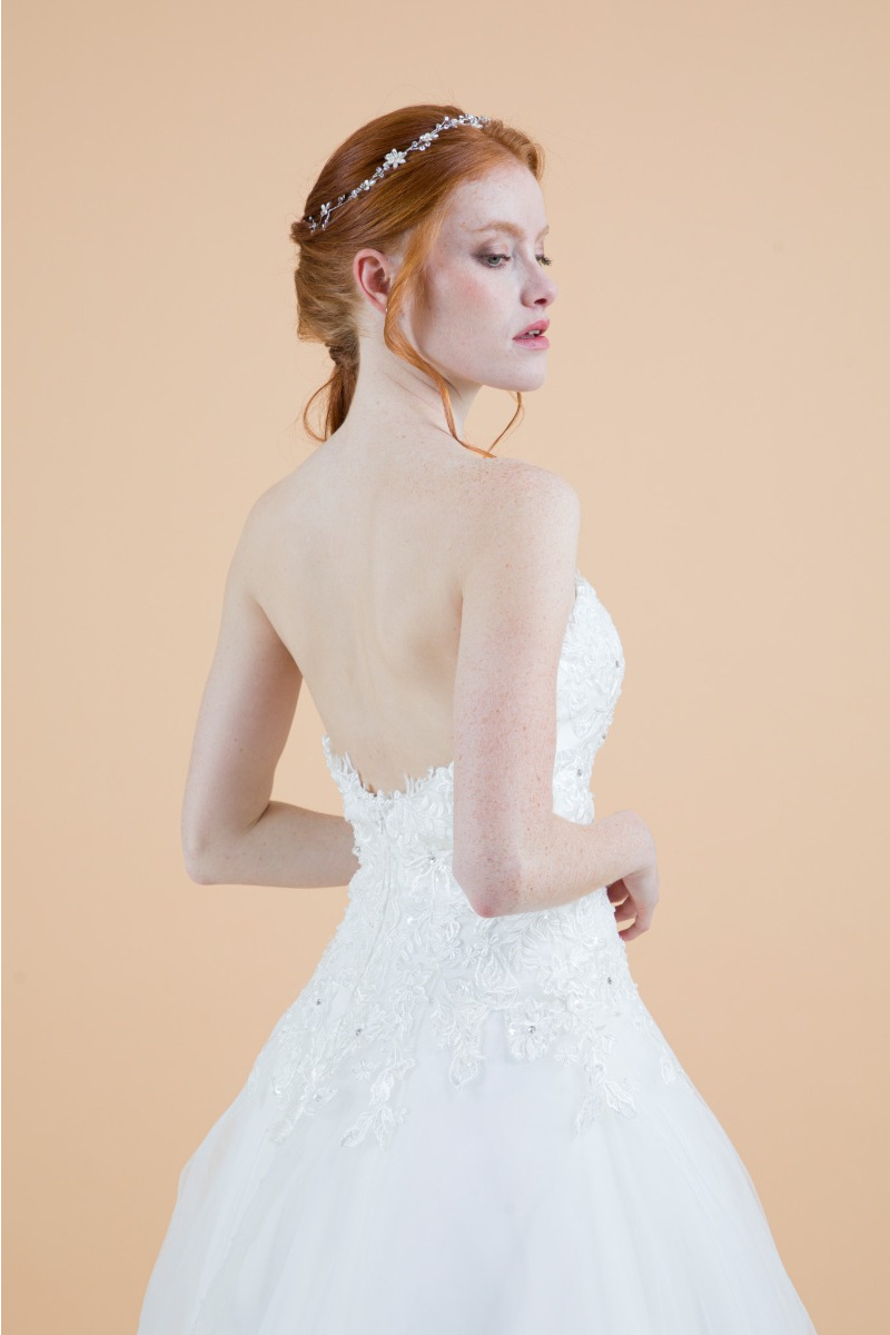 Abito da sposa fiordaliso, spalle scoperte, dettagli floreali, sfondo beige.
