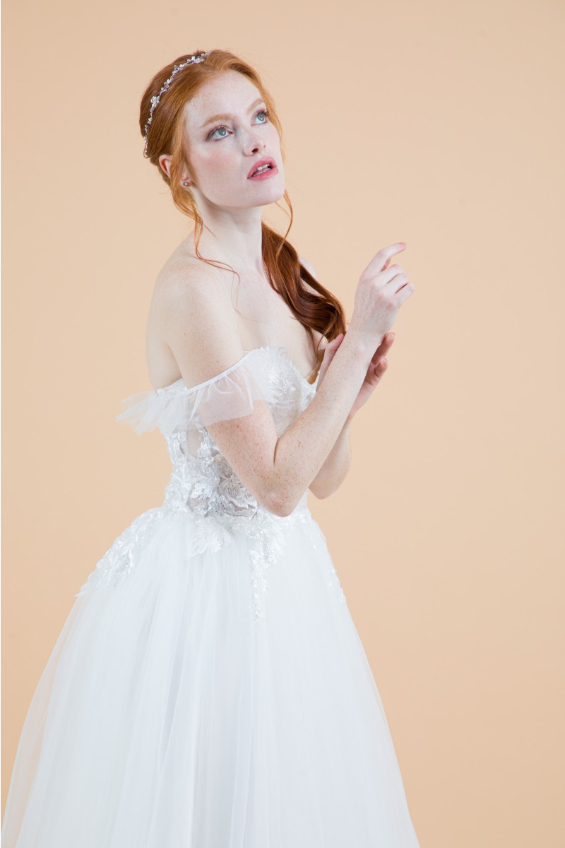 Abito da sposa Dalia con dettagli in pizzo e spalle scoperte, sfondo neutro.