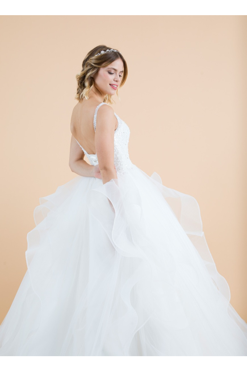 Abito da sposa Biancospino in tulle bianco con spalline sottili e dettagli floreali, sfondo beige.