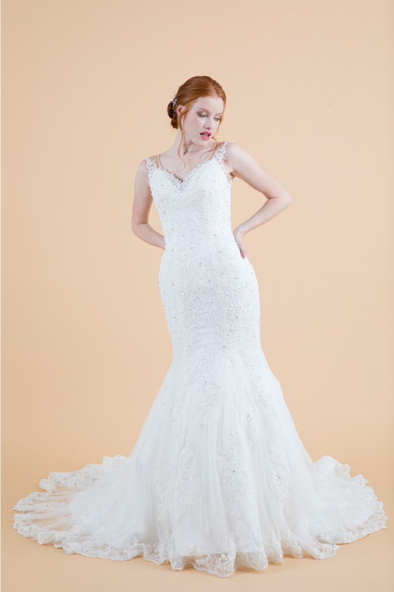 Abito da sposa Agatea in pizzo bianco con strascico, modello sirena, sfondo beige.