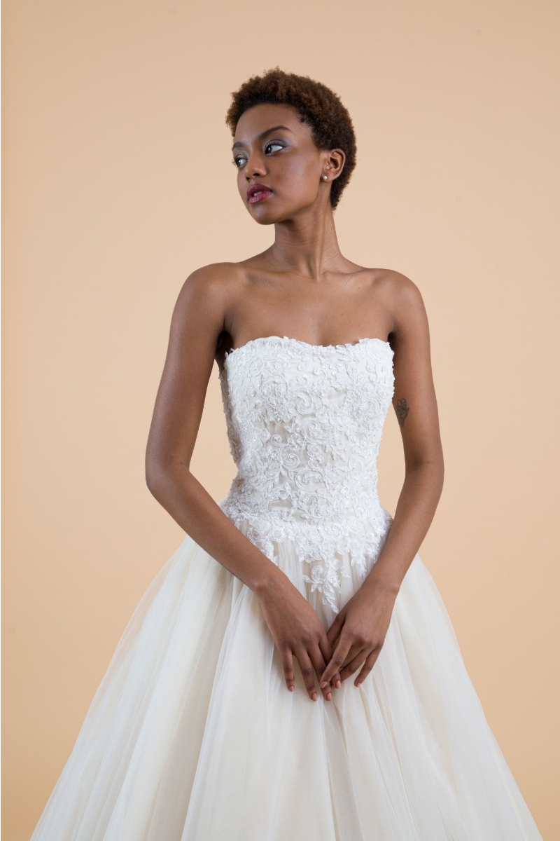 Abito da sposa Campanula in pizzo bianco, senza spalline, su sfondo beige.
