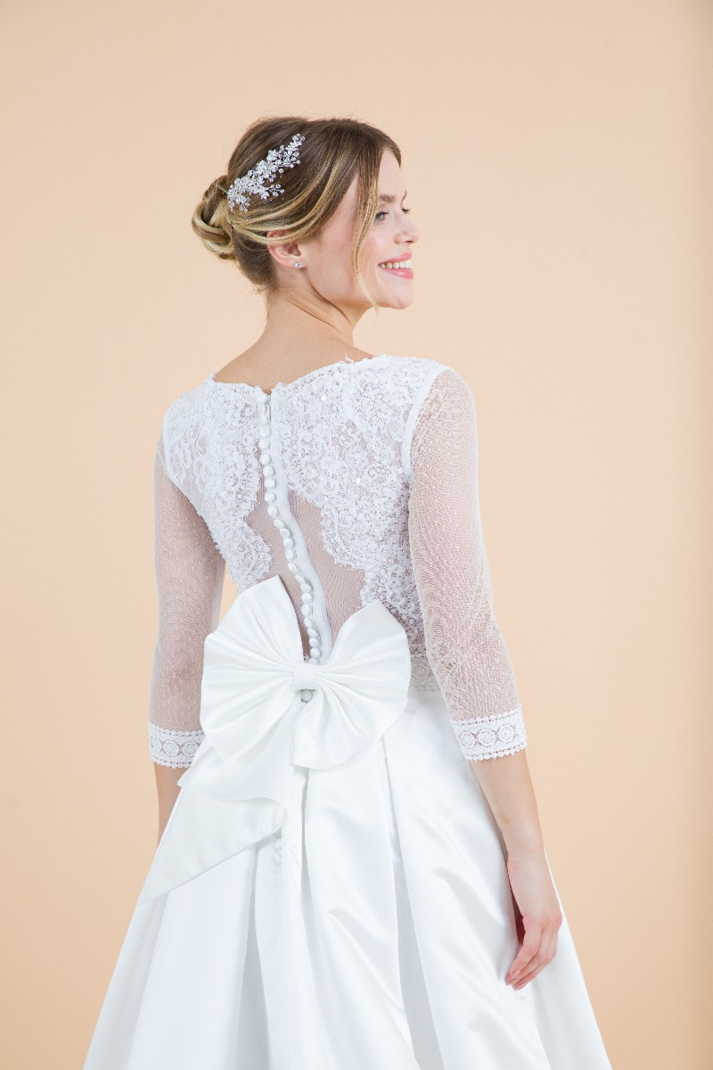 Abito da sposa Silene in pizzo bianco con fiocco, vista posteriore, modella sorridente.