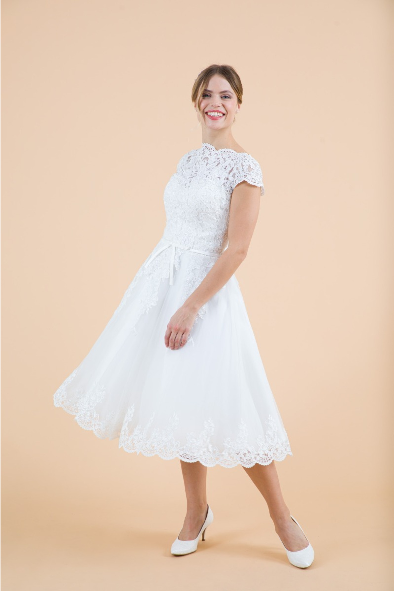 Abito da sposa giglio in pizzo bianco, lunghezza midi, maniche corte, indossato da modella sorridente.