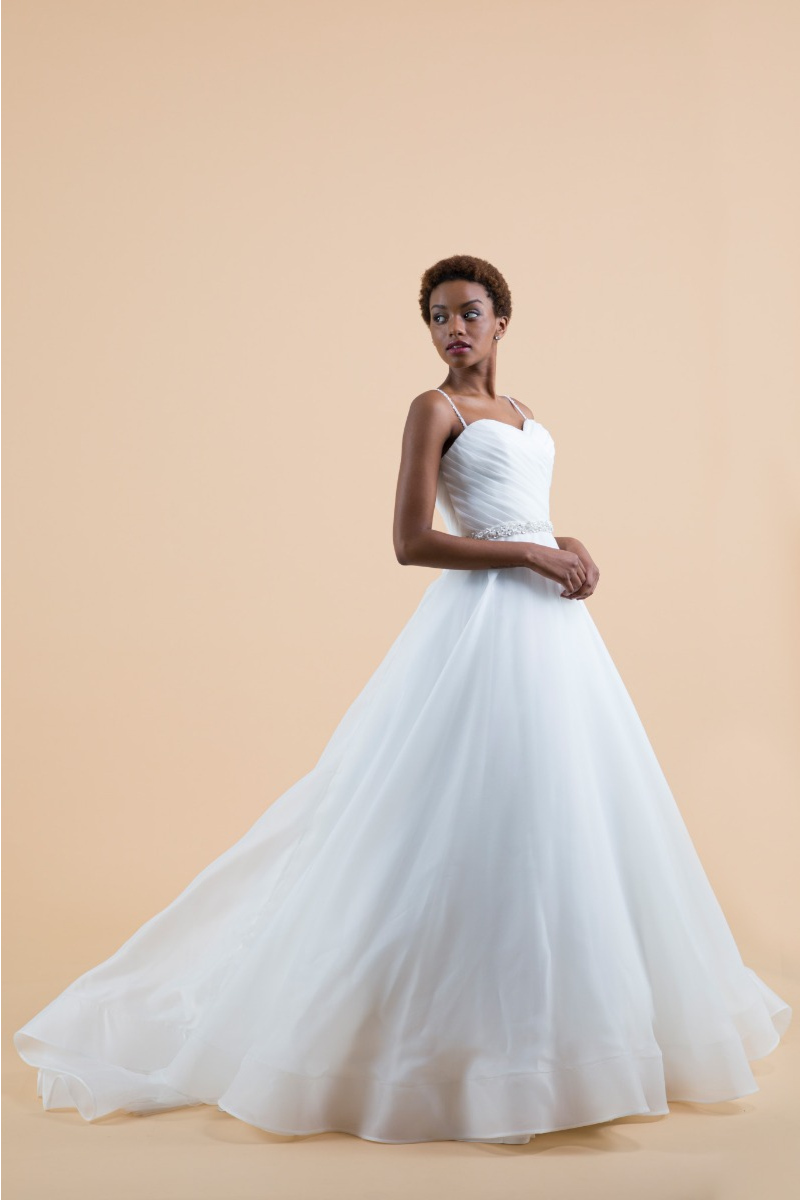 Abito da sposa calla bianco con spalline sottili, gonna ampia, sfondo beige.