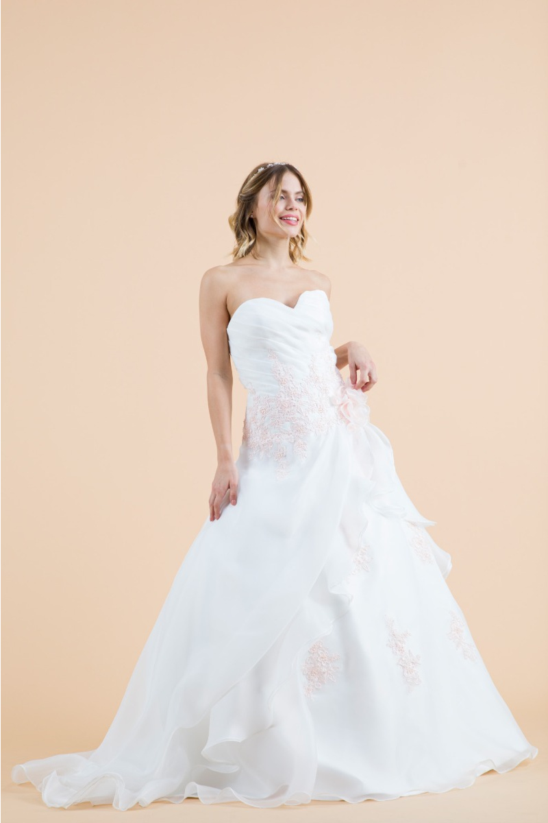 Abito da sposa ginestra bianco con dettagli floreali, scollo a cuore, sfondo beige.