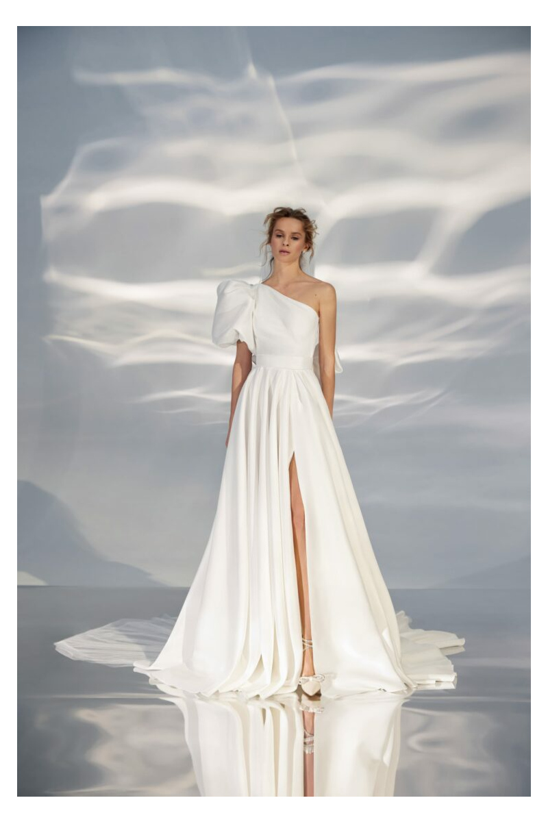 Abito da sposa bianco monospalla con spacco, modello L320 Ariamo Light, sfondo effetto onde di luce.