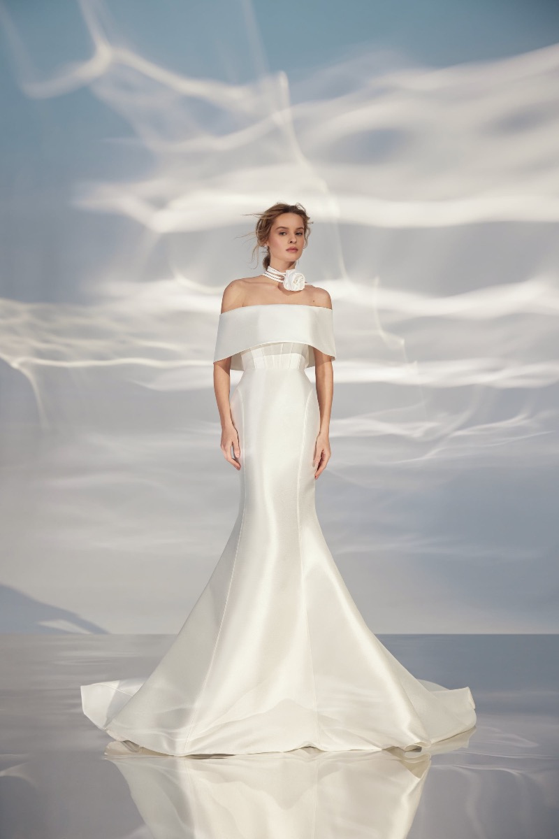 Abito da sposa bianco ARIAMO LIGHT L321 con scollo a barca e decorazione floreale, sfondo celeste.