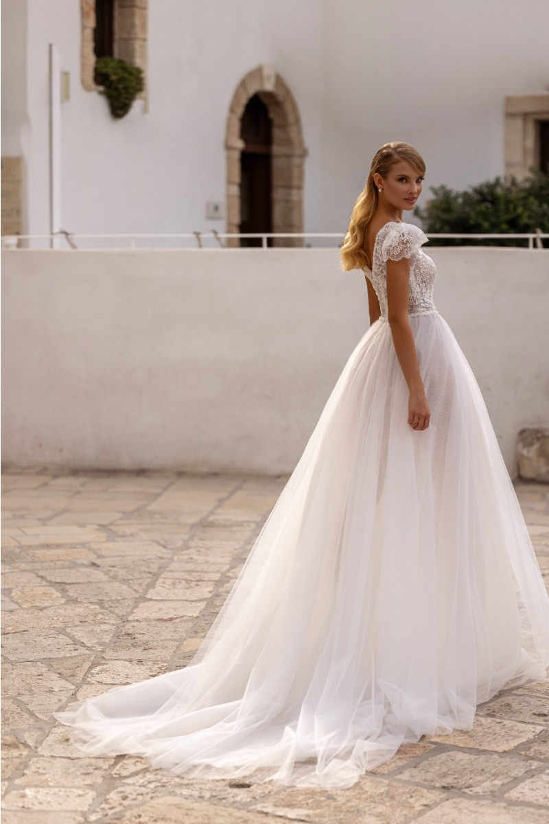 Abito da sposa LANTHANA - MADIONI in pizzo e tulle con strascico, ambientato in un cortile elegante.