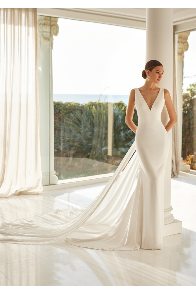 Abito da sposa LILIBET elegante con strascico, scollo a V, in un ambiente luminoso con vista sul giardino.