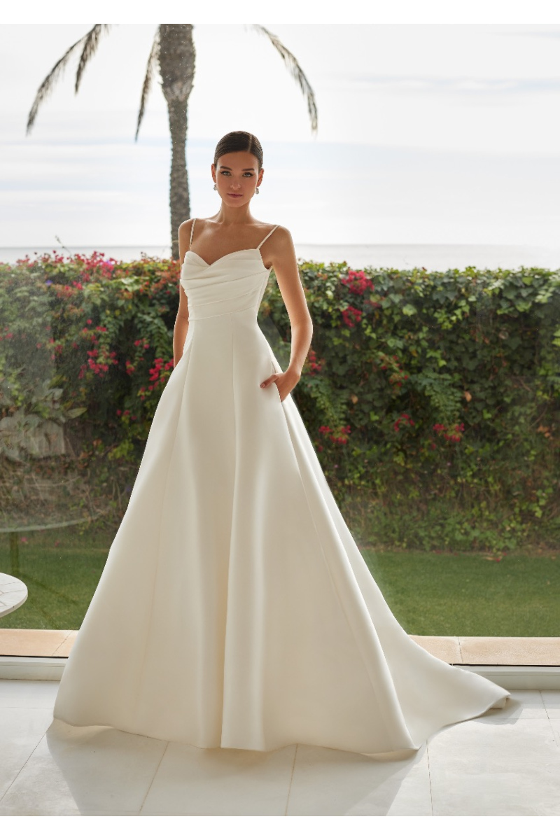 Abito da sposa LYLA St. Patrick, elegante con spalline sottili, sfondo tropicale.