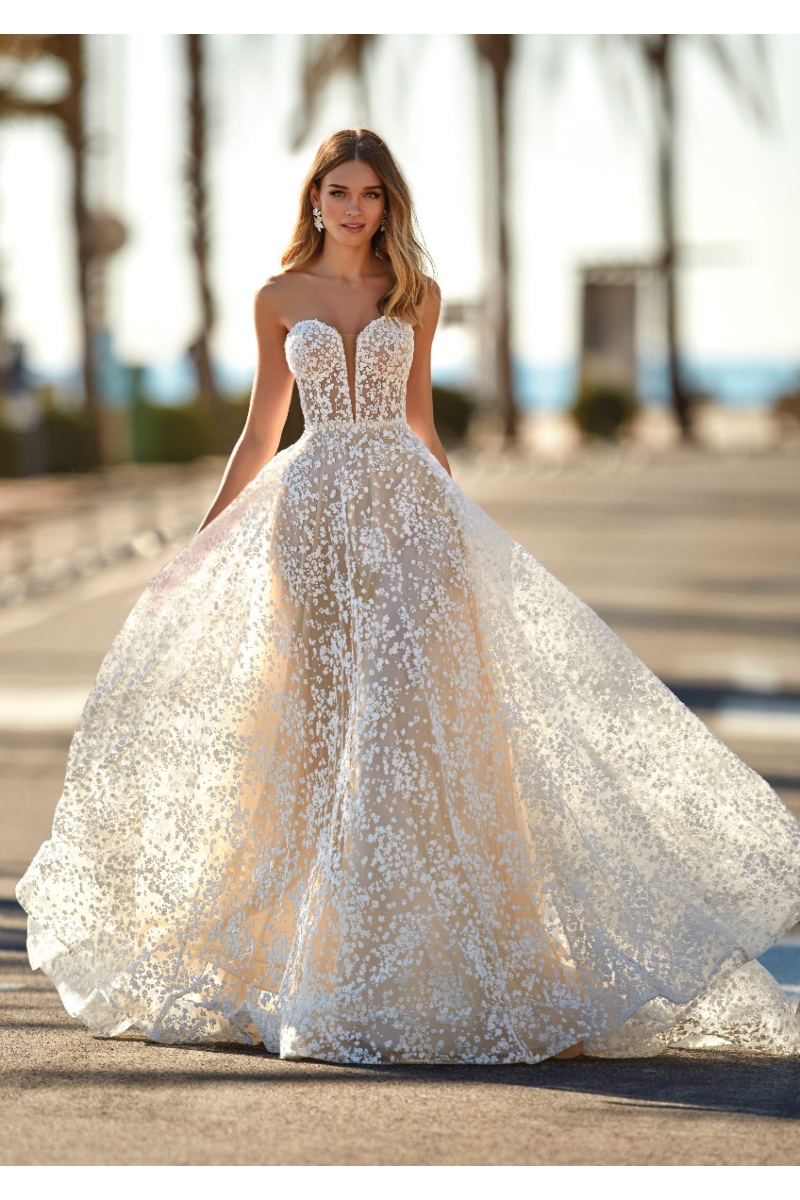 Abito da sposa MINDY con corpetto ricamato e gonna ampia, sfondo esterno con palme.