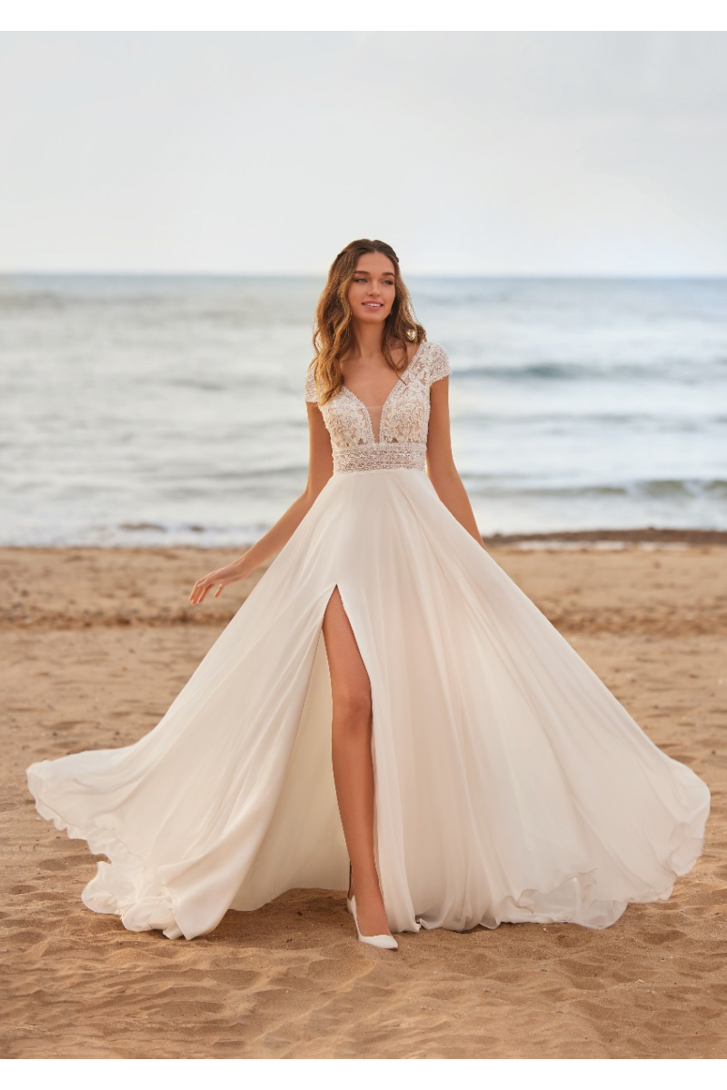 Abito da sposa MINNIE St. Patrick in pizzo e chiffon bianco, scollo a V, spiaggia sullo sfondo.