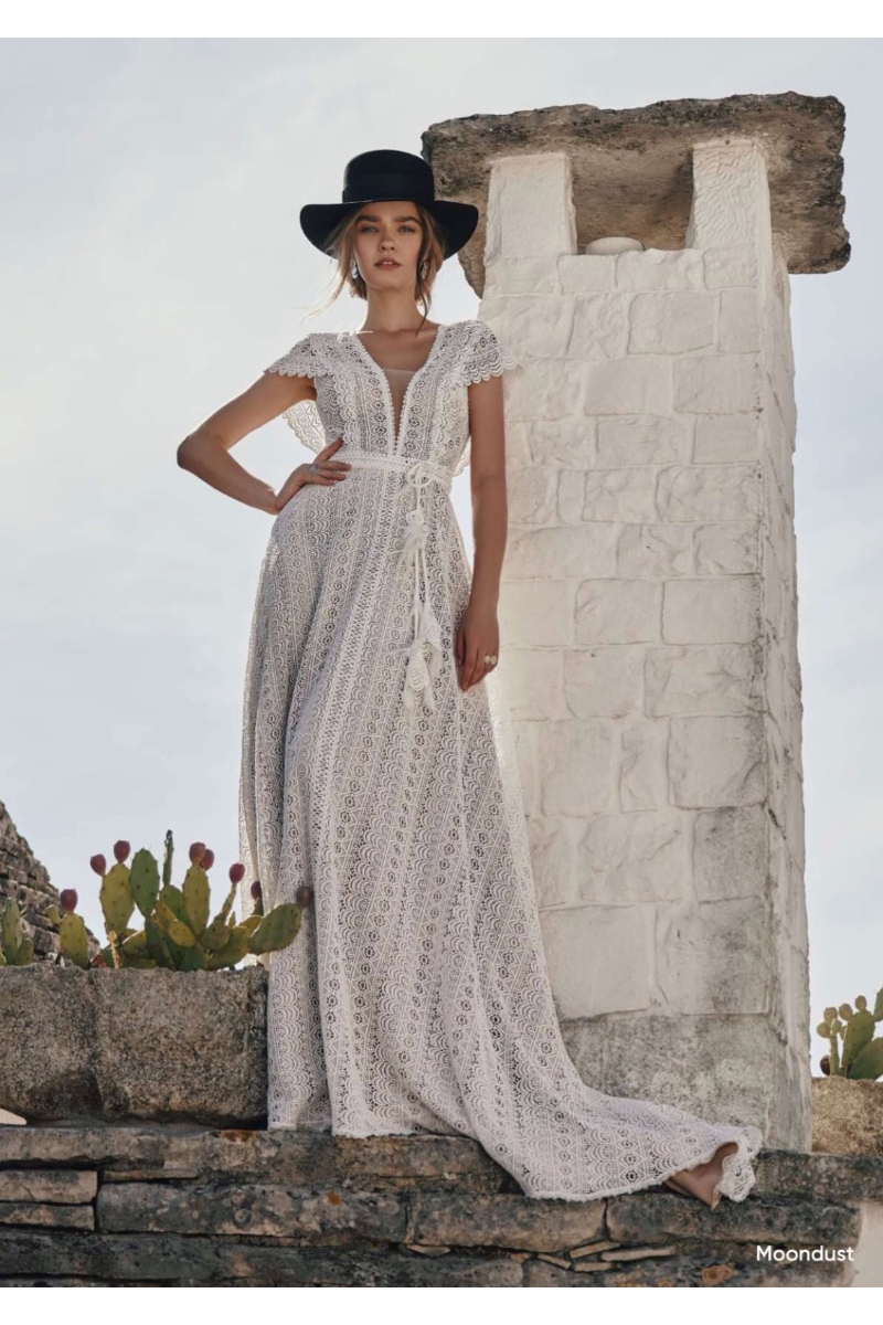 Abito boho in pizzo bianco Moondust di Ariamo, indossato da modella con cappello nero, sfondo rustico.