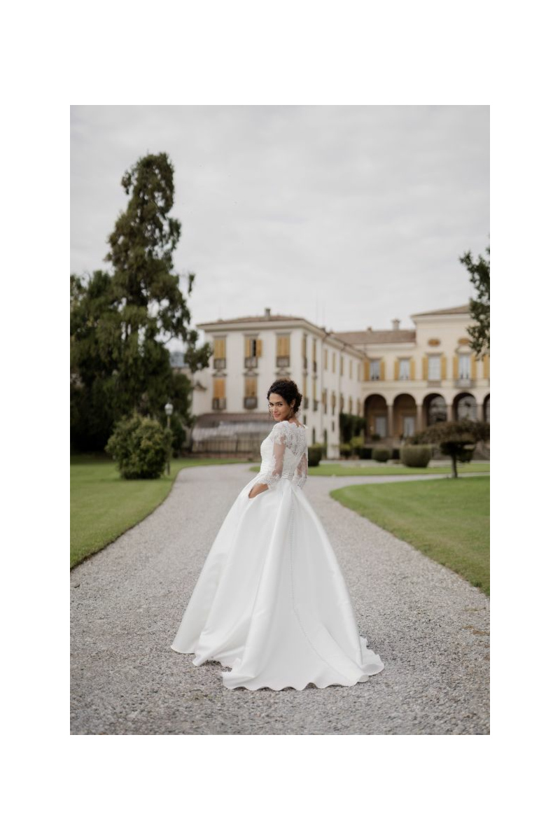 Abito da sposa ASTREO di Sposae Atelier, donna in giardino con edificio storico sullo sfondo.