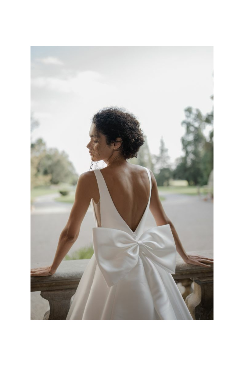 Abito da sposa GINEVRA Sposae Atelier con schiena scoperta e grande fiocco, ambientato in giardino.