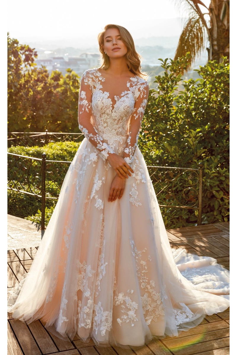 Abito da sposa Nessa di Eddy K con pizzo floreale e maniche lunghe, ambientato in un giardino soleggiato.
