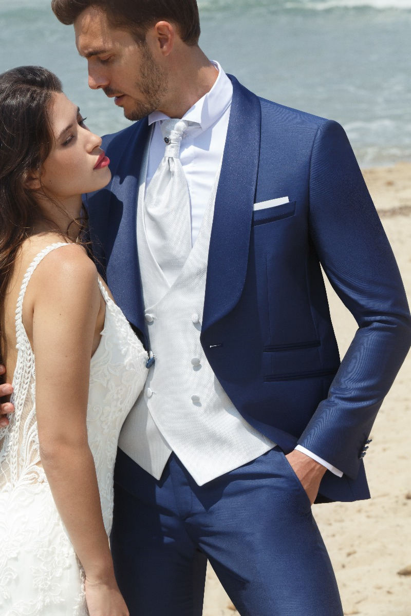 Abito elegante uomo blu PALAZZO C8 148, con giacca e gilet bianco, su spiaggia.