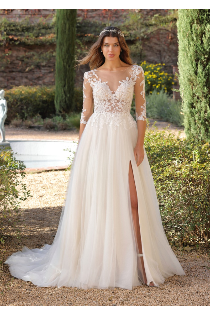 Abito da sposa Pavi Ladybird in pizzo floreale, scollo a V, maniche lunghe, spacco laterale, sfondo giardino.