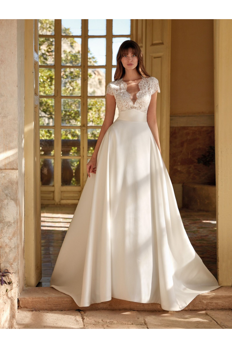 Abito da sposa RHODA di Nicole Colet con corpetto in pizzo e gonna ampia, ambientato in un elegante interno rustico.