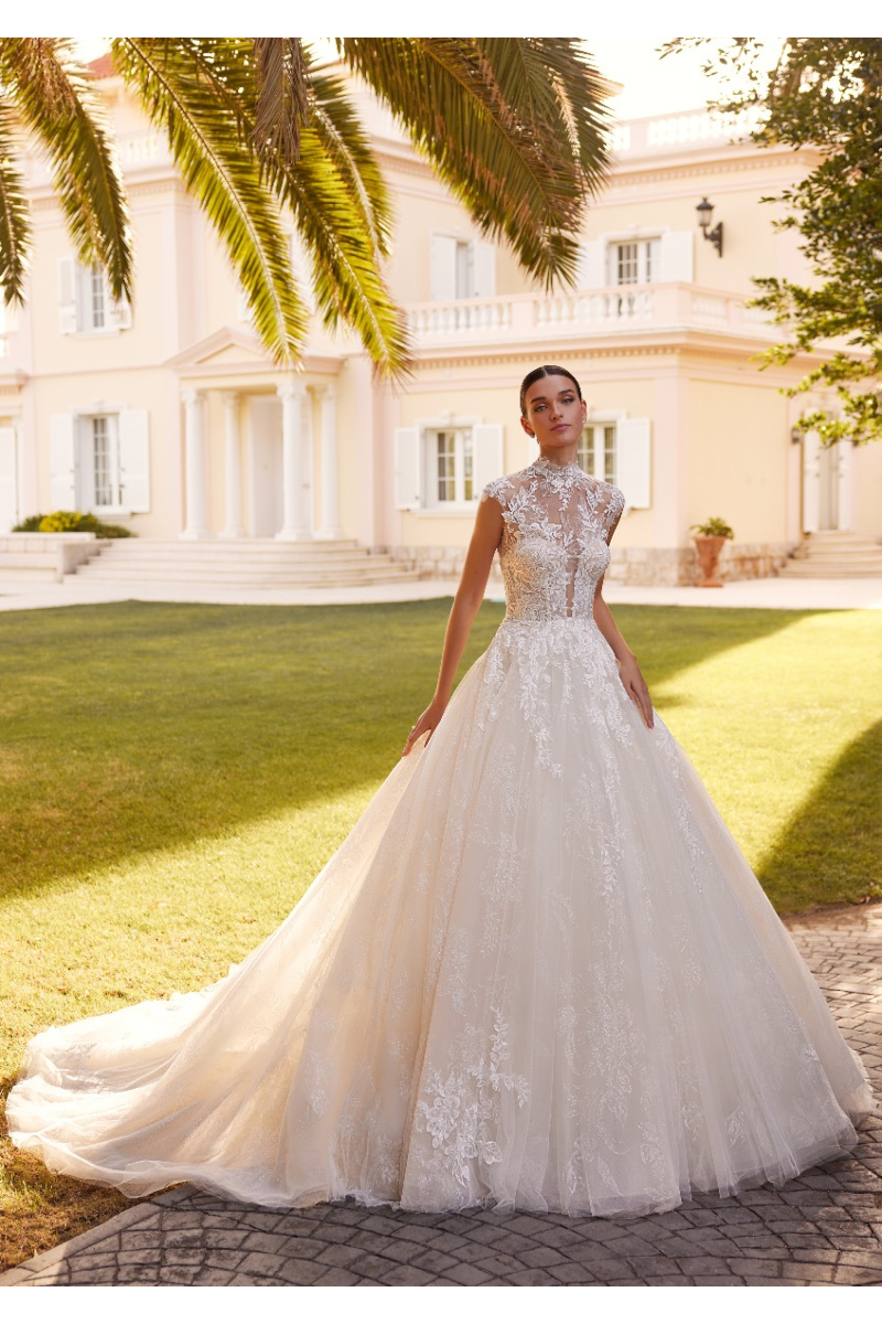 Abito da sposa ROYALE in pizzo, sfondo villa elegante e palme.