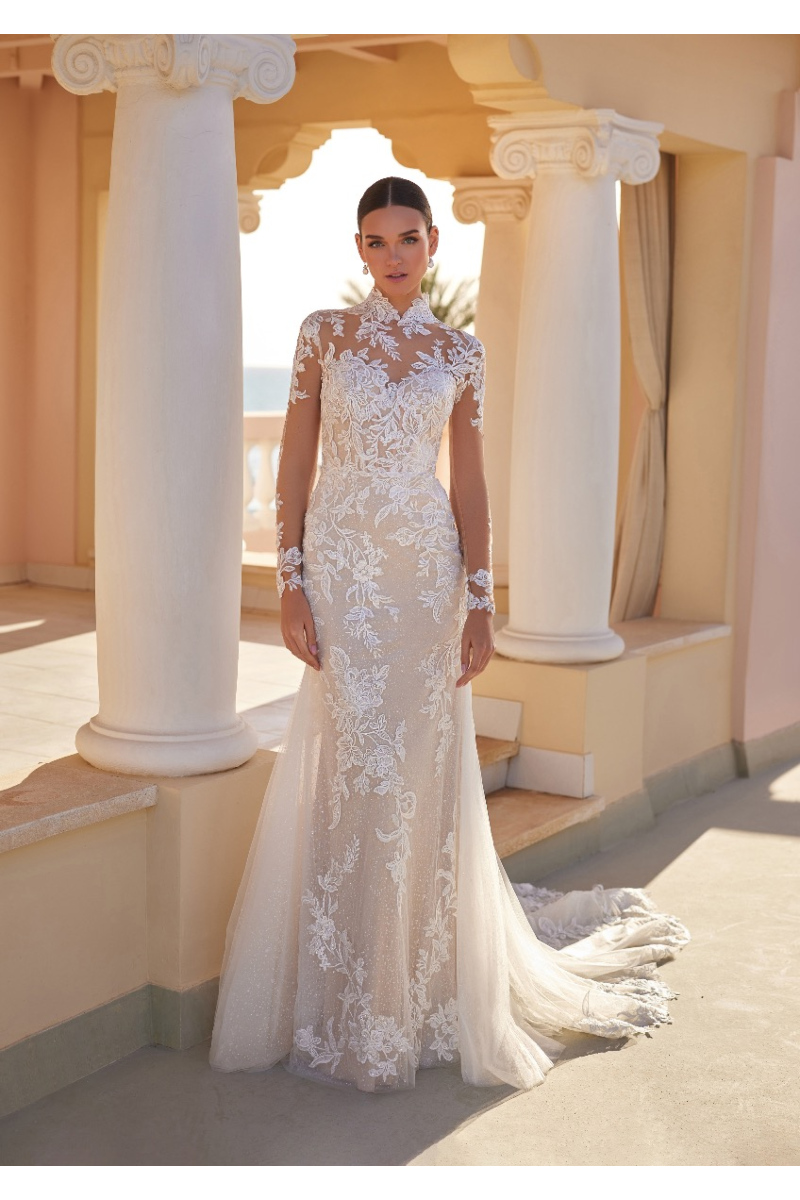 Abito da sposa SIANNA St. Patrick in pizzo avorio, maniche lunghe, scollo alto, sfondo colonne eleganti.