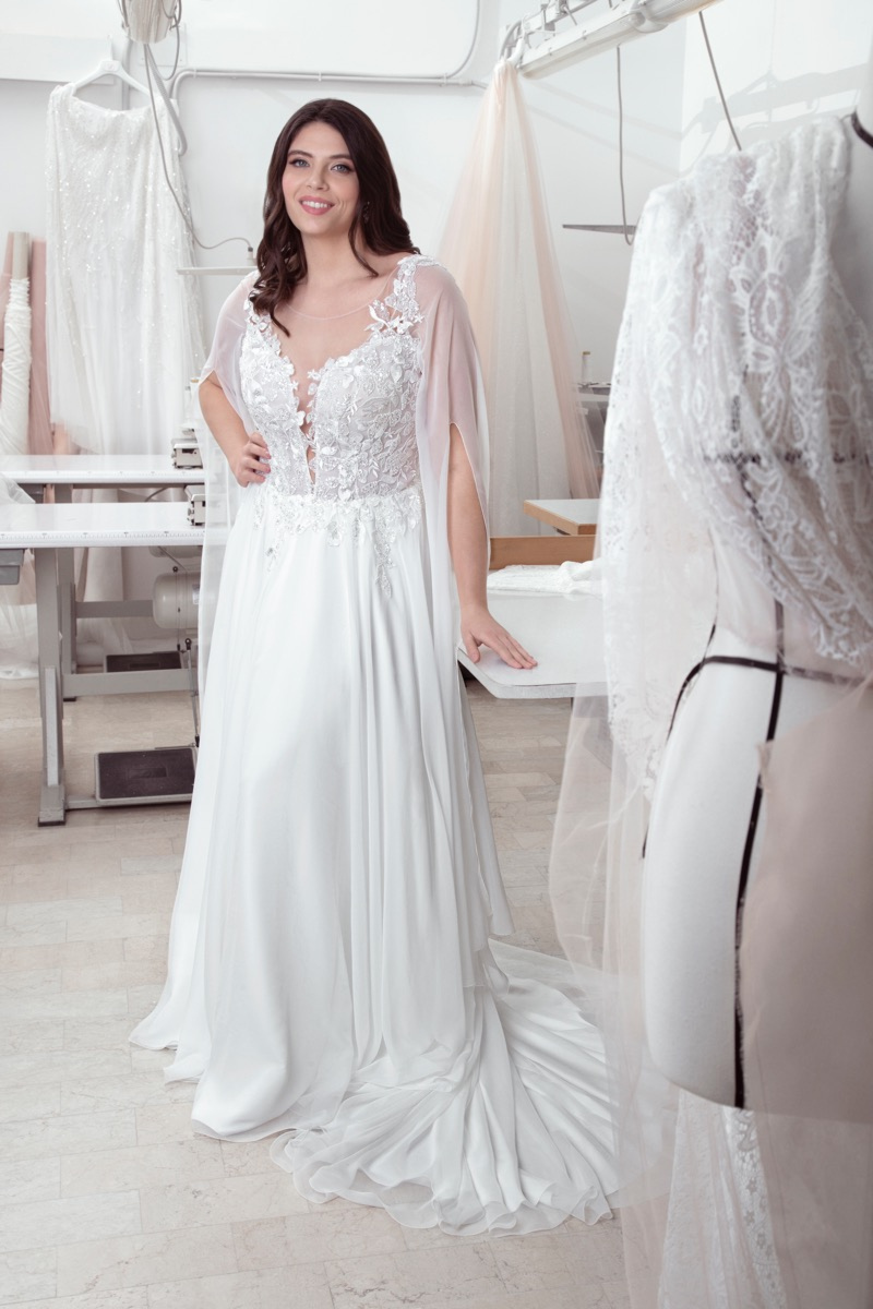 Abito da sposa curvy MEGAN con dettagli in pizzo, modella sorridente in atelier sartoriale.