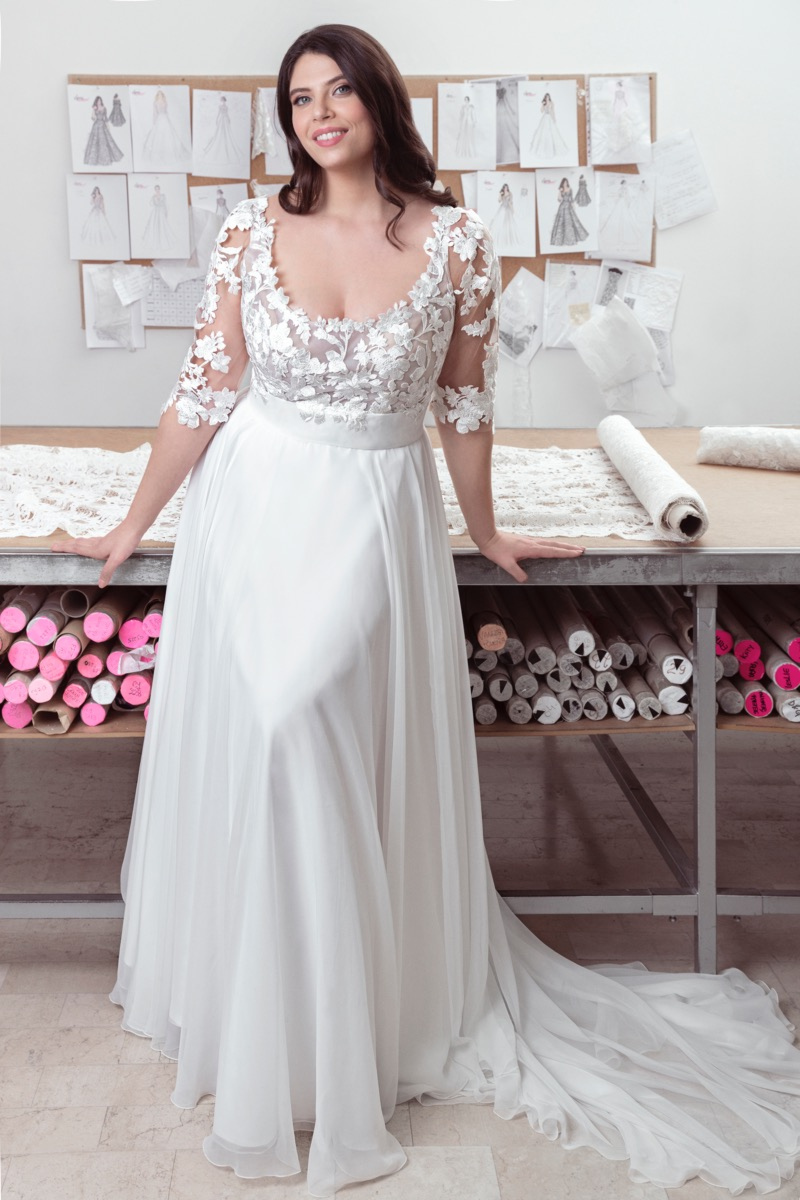 Abito da sposa curvy Chiara in pizzo floreale, maniche a 3/4, sfondo con bozzetti di moda.
