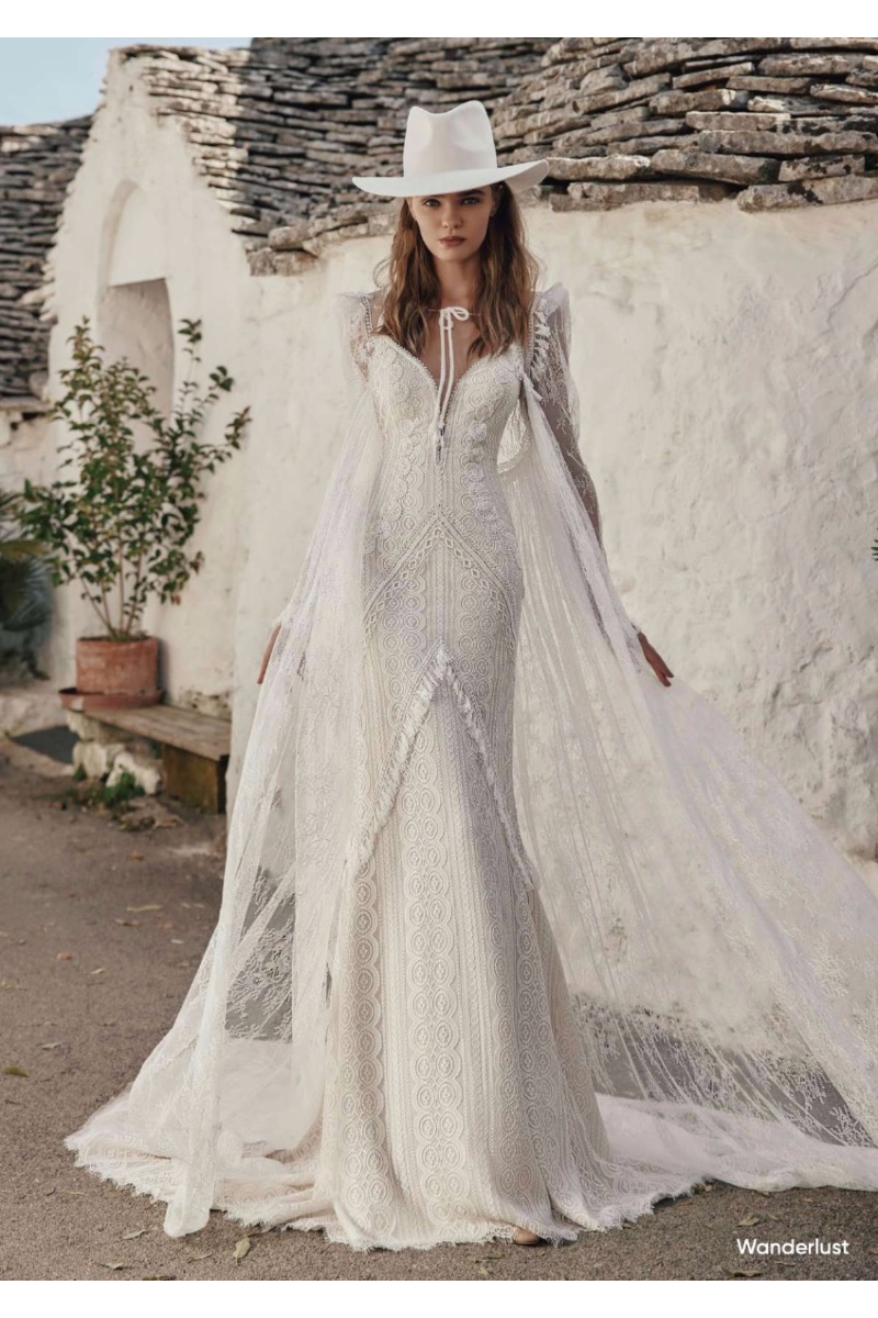 Abito da sposa boho Wanderlust Ariamo con cappello bianco, sfondo rustico.