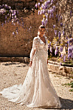 Abito da sposa ASAMI - DAMA in pizzo floreale, sfondo con glicine in fiore e muro antico.