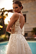 Abito da sposa BEATRIX - DAMA con dettagli floreali in pizzo, sfondo piscina e palme.