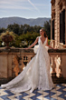 Abito da sposa CHARLOTTE - DAMA, elegante con scollo a V, sfondo villa storica e paesaggio montano.