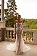 Abito da sposa PROCELLA - DAMA in pizzo floreale, spalle scoperte, su balcone con vista su giardino.