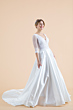 Abito da sposa Silene in raso bianco con maniche trasparenti e gonna ampia, sfondo beige.