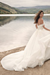 Abito da sposa Maggie Sottero Knox, scollatura a spalle scoperte, lungo strascico, ambientazione naturale vicino a un lago.