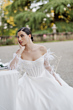 Abito da sposa AKOYA-Romantica by Sposae con dettagli di perle e piume, ambientato in un giardino elegante.