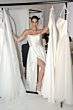 Modella in abito bianco elegante, collezione Ludovica Essential Everlasting, tra abiti su appendiabiti.