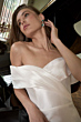 Abito bianco elegante KIKI - THE ROMANTICA COLLECTION, indossato da modella vicino a un pianoforte.