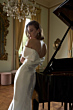 Abito elegante bianco KIKI - The Romantica Collection, donna accanto a pianoforte in sala lussuosa.