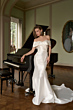 Abito da sposa elegante in raso bianco, collezione KIKI Romantica, accanto a un pianoforte a coda.
