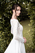 Abito da sposa in pizzo bianco, collezione Taissa, sfondo di foglie verdi.